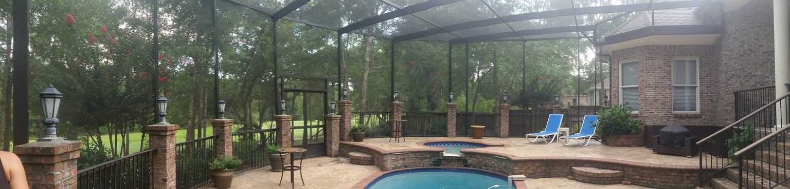 Panoramic pool enclosure beside a brick home with raised terrace and landscaping